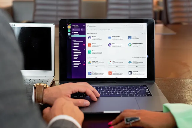 Two professionals collaborating using laptops and communication software in a business setting. What questions do sales enablement teams ask most often?