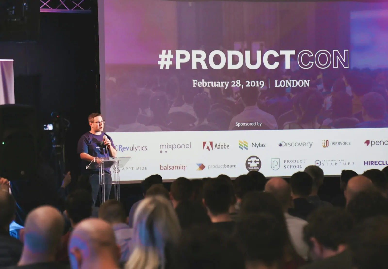 man speaking on stage a man standing on stage behind a podium giving a presentation at an event. The practical 2027 guide to customer adoption