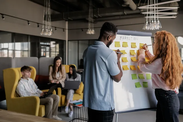 Team collaborating in a modern office, planning strategy on a whiteboard, young adults working together. How to screen product marketing strategy case studies