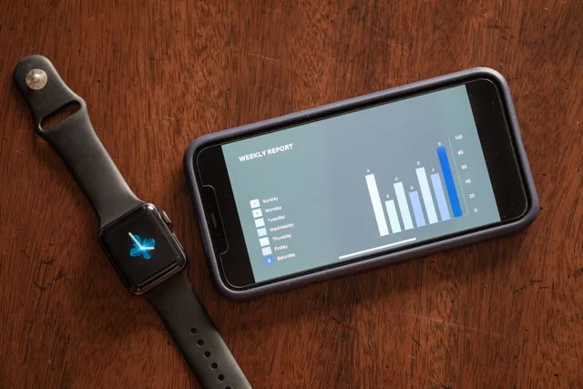 Close-up of a smartphone and smartwatch displaying a weekly report on a wooden table. Positioning and adoption tools for product marketing