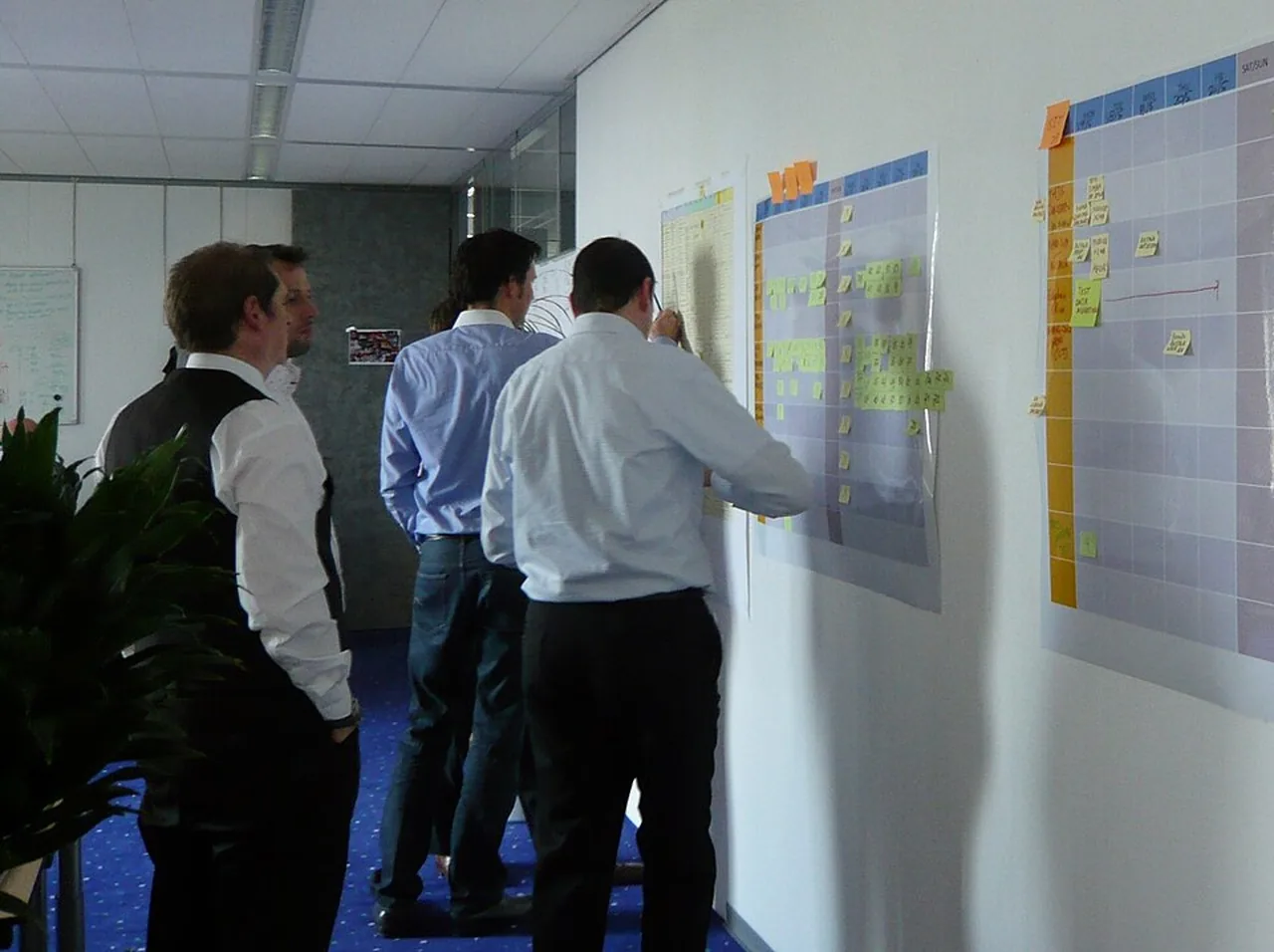 Four people review tasks on wall-mounted planning boards covered with notes.